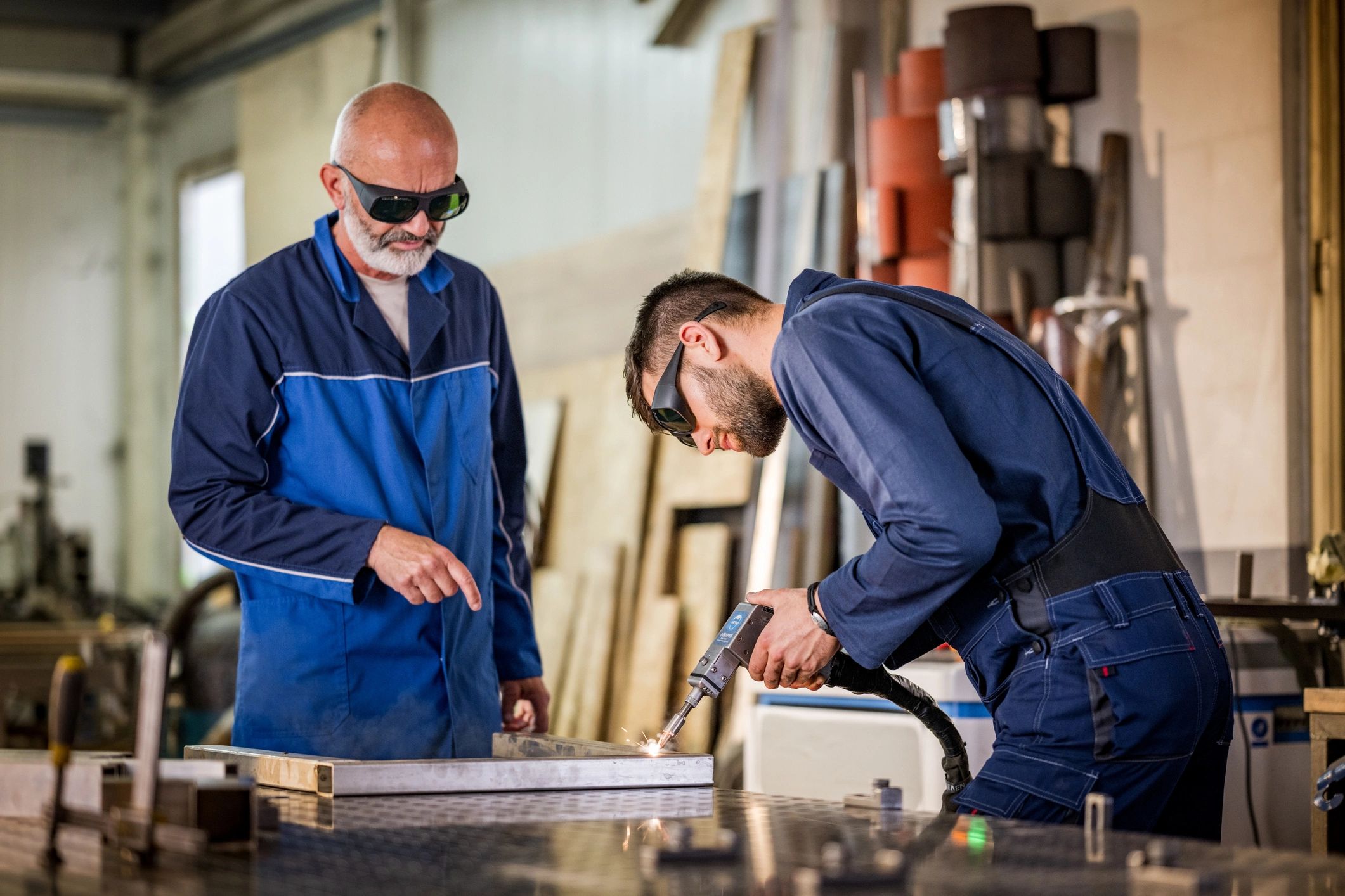 Instructor supervising a trainee using welding equipment in an industrial workshop